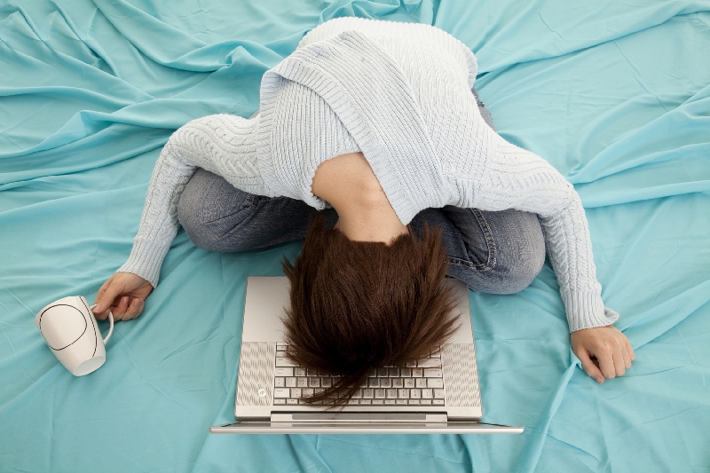 woman slouched over computer with coffee cup in hand