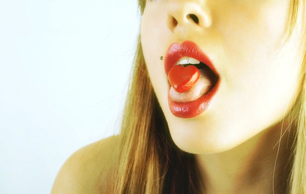 Red pill shaped like a heart on a young woman's tongue, on a white background