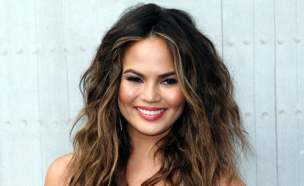 chrissy teigen posing in front of gray background smiling
