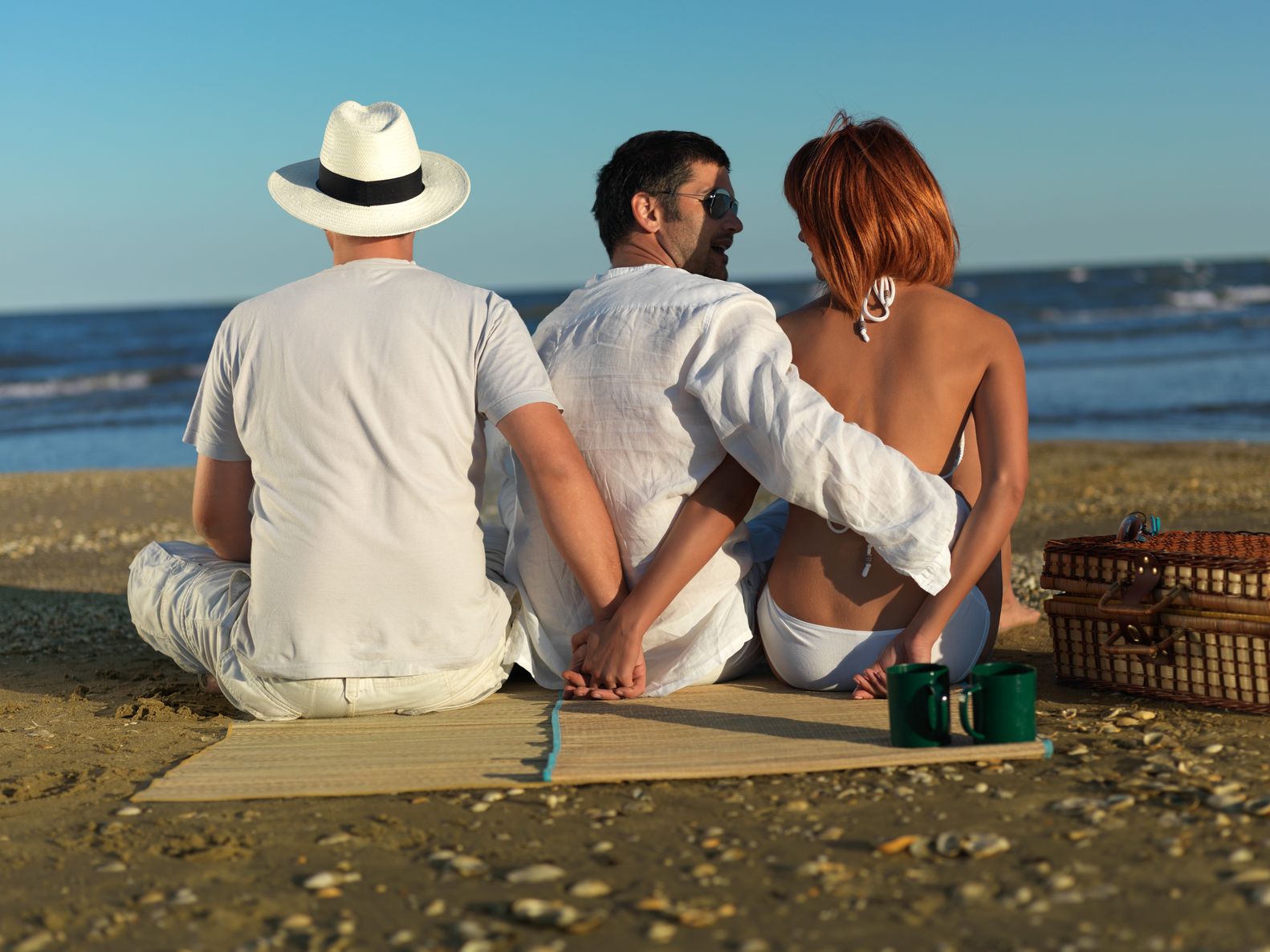 16038750 - young woman talking with the boyfriend, while holding hands with another man, at a picnic by the sea shore