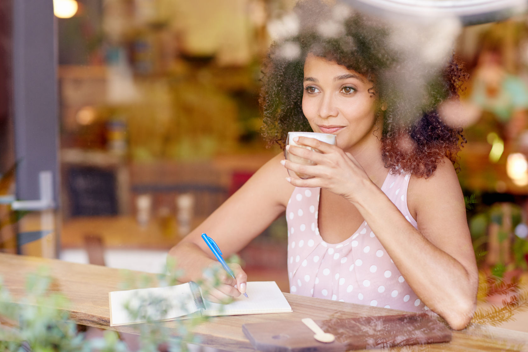 51356875 - beautiful mixed race woman sitting in a coffee shop sipping her latte and daydreaming while gazing out of the window