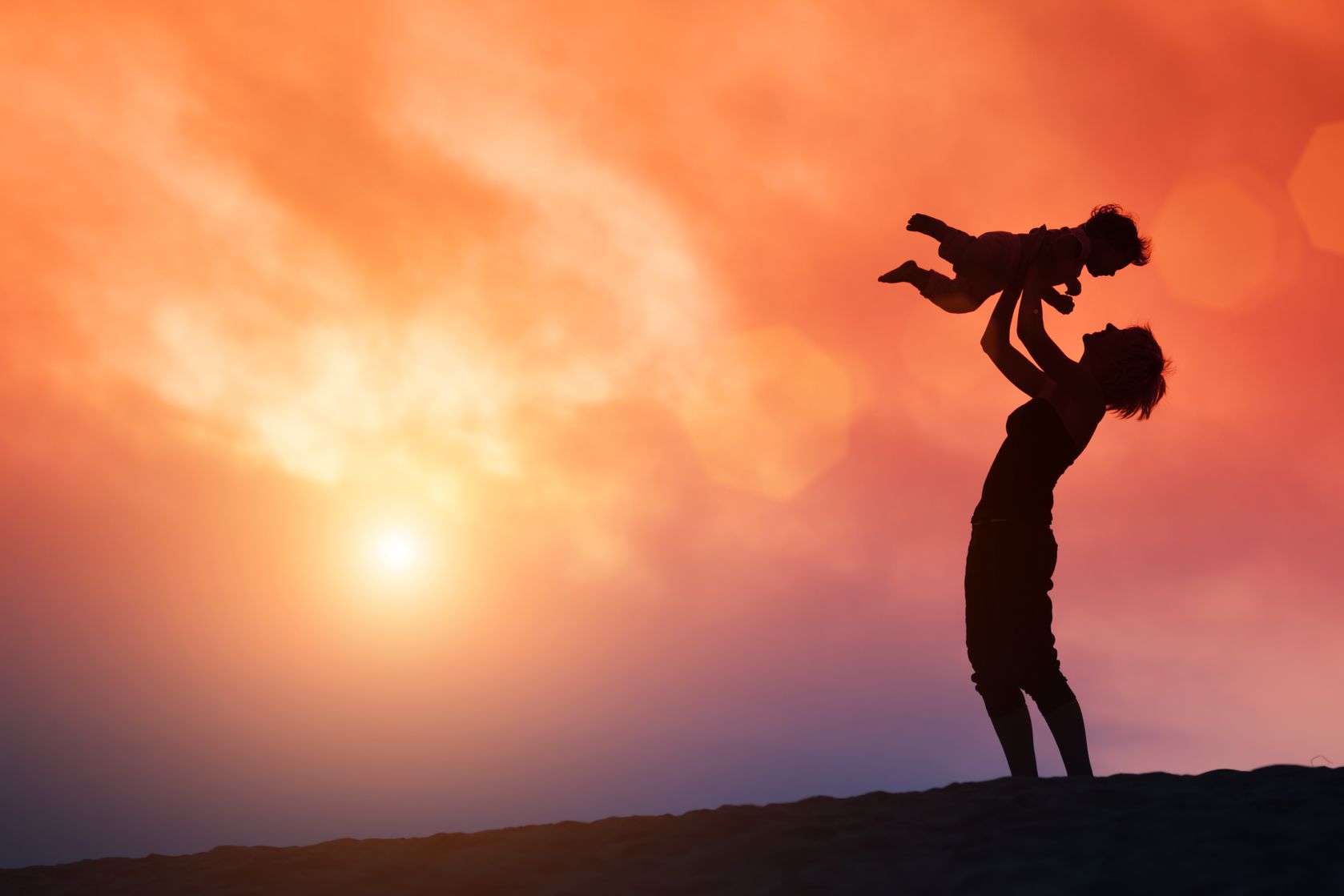 18709037 - mother lifting toddler child in air over scenic sunset sky
