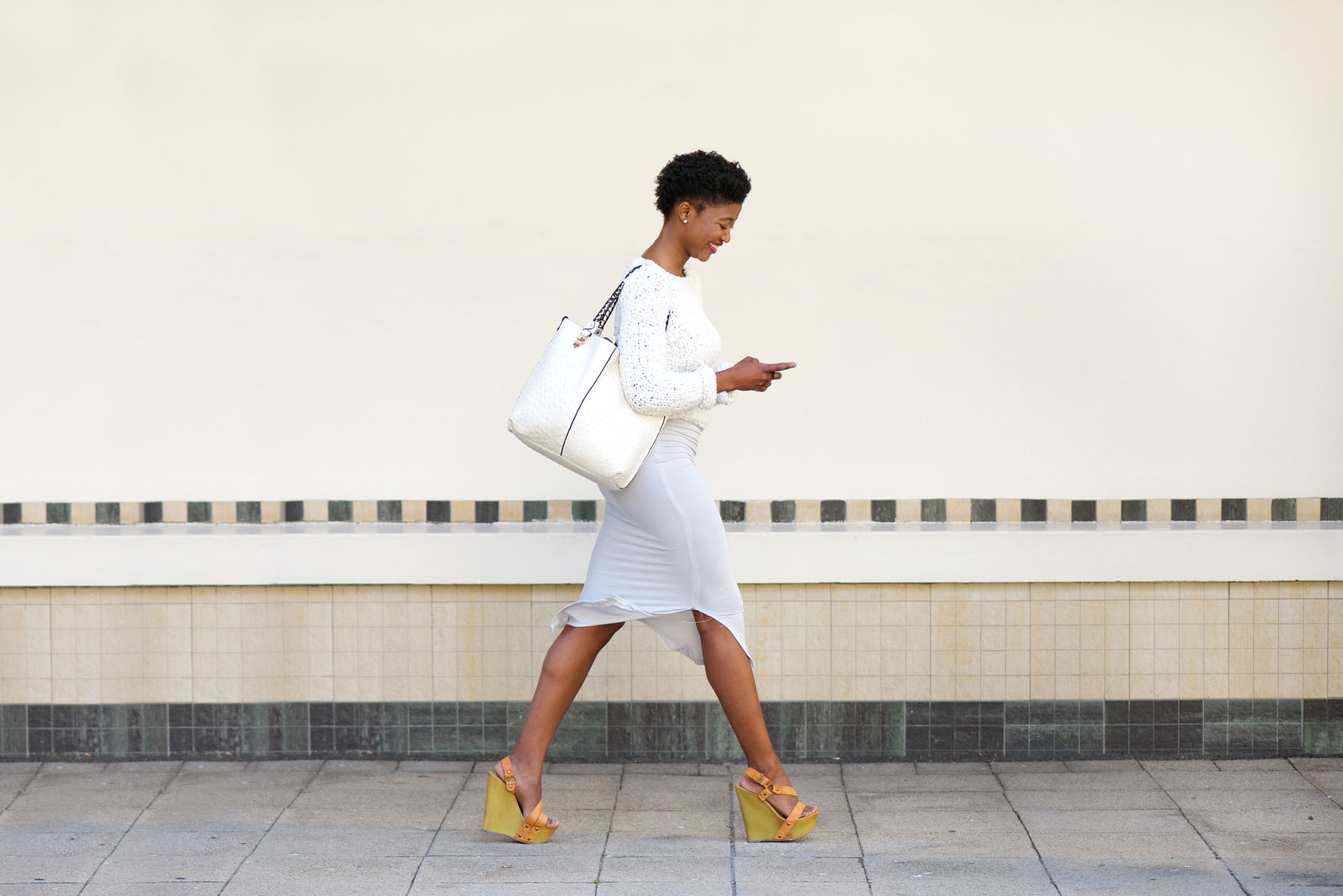 36328180 - full length side portrait of a young woman walking and sending text message on cell phone